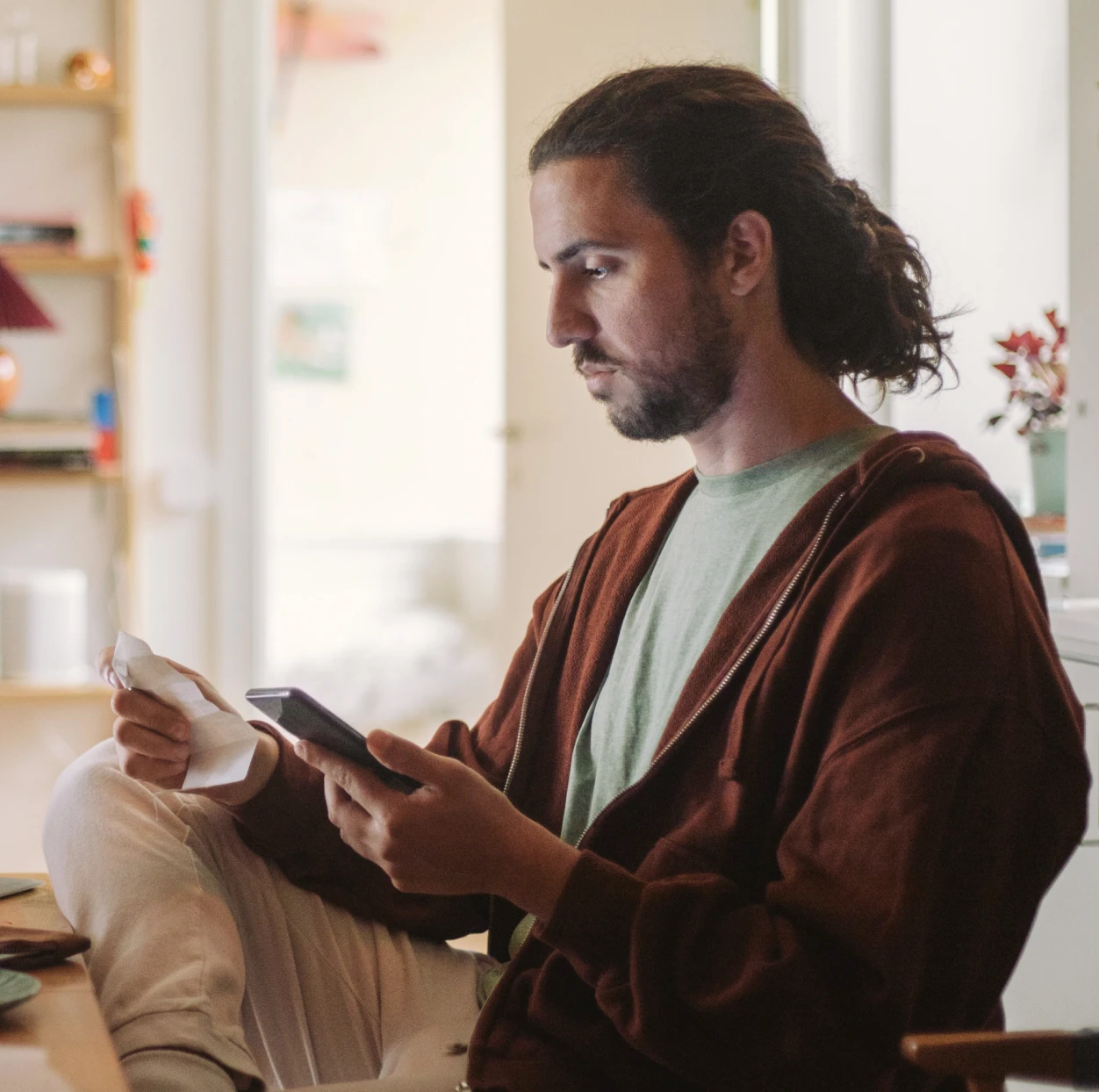 Man working at his desk looking at his phone and a receipt